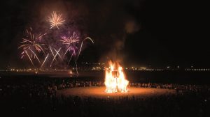 Fiestas tradicionales de Asturias: Noche de San Juan 2022 Hoguera de San Juan (San Xuan) en Gijón con fuegos artificiales de fondo - Turismo Rural Asturias